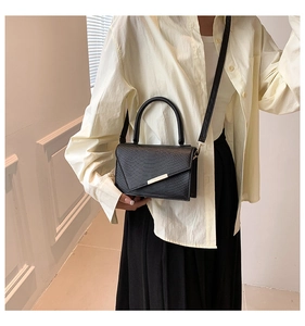 Close-up of black crocodile embossed handbag with silver trim on model in soft indoor light