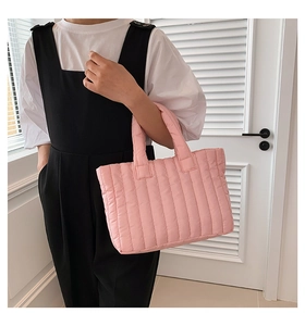 Detail of pink vertical quilted puffer tote bag with soft padded handles shown held by hand