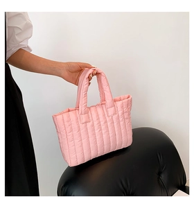 Detail of light pink quilted handbag featuring vertical padded stripes and soft texture