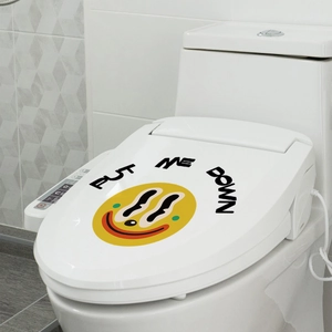 Détail d'un autocollant WC smiley jaune avec texte Put Me Down sur abattant blanc