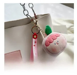 Close-up of a plush peach bag charm with Sweet strap and golden ring on a white tote bag