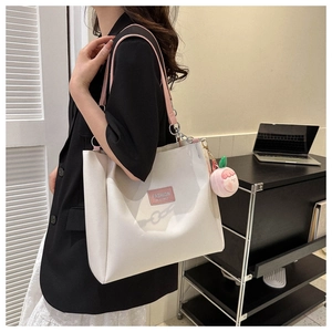 Detail of white tote bag featuring pink straps and a cute peach plush charm pendant