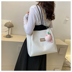 Rear view of model wearing white PU tote bag with chain strap and peach plush charm