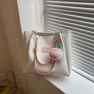 Detail of cream tote bag with pink handles, featuring a peach plush charm and text detail