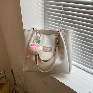 Detail view of a cream PU tote bag with a pink peach charm and silver chain on a windowsill