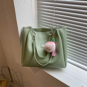 Detail of light green tote bag with silver chain handle and pink peach plush pendant