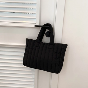 Detail van zwarte gewatteerde shopper met verticale stiksels hangend aan een handvat