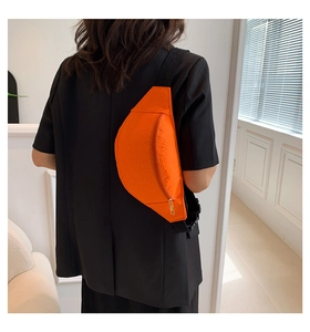 Detail view of bright orange crocodile embossed chest bag with gold zipper and strap