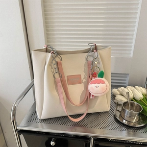 Fashionable cream white tote bag with pink straps and cute cartoon charm on a metal shelf