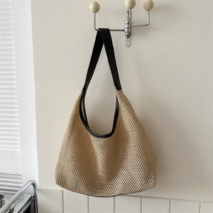 Minimalist woven straw tote bag with black leather straps hanging on a neutral wall hook