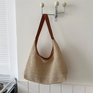Minimalist woven straw tote bag with brown leather straps hanging on a white wall