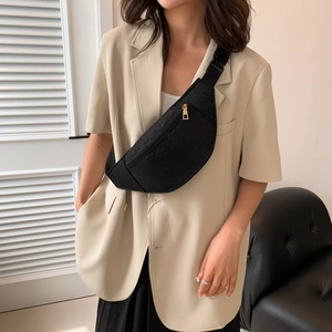 Chic black embossed chest bag with gold zipper worn crossbody over a beige blazer