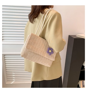 Dettaglio borsa a spalla in paglia intrecciata con fiore viola e manici in corda