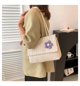 Dettaglio di borsa tote in paglia beige con fiore viola all'uncinetto indossata