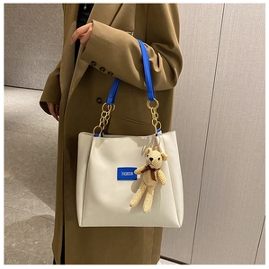 Close-up of beige tote with blue leather strap and adorable knitted bear charm