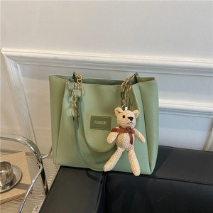 Green faux leather tote bag with gold chain strap and bear pendant on white background