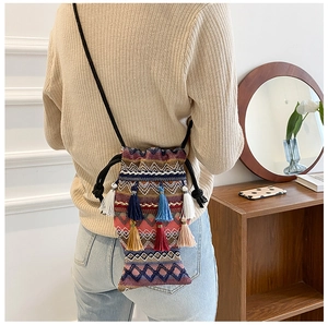 Detailansicht der Bohème-Stricktasche in Fischform mit bunten Quasten auf beigem Pullover