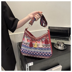 Close-up of bohemian woven shoulder bag featuring colorful tassels and wide patterned strap