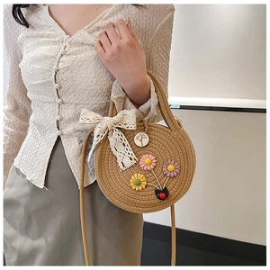 Détail d'un sac rond en paille tressée avec fleurs 3D colorées et nœud en dentelle