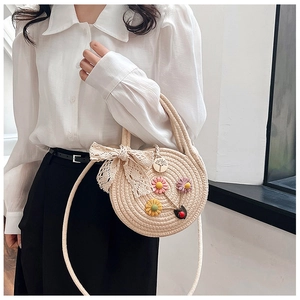 Détail du sac rond en paille avec broderie florale, nœud en dentelle et bandoulière réglable