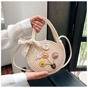Détail du sac rond tressé avec décorations florales, nœud en dentelle et poignées