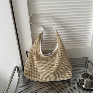 Detail of hand-woven straw hobo bag with white leather strap on a minimalist metal rack