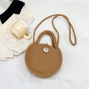 Dettaglio di una borsa intrecciata marrone con bottone in legno su sfondo di tessuto bianco