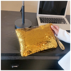 Close-up of golden sequin clutch with wristlet strap held by woman in a white blazer