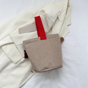Dettaglio della borsa in lino kaki con manico rosso vivace e nappe bordeaux eleganti