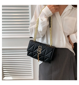 Detail of black quilted shoulder bag with gold chain strap and tassel on a female model