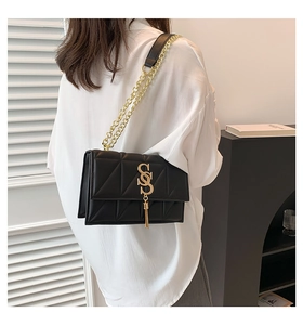Detail view of black quilted crossbody bag with gold metal S logo and chain tassel strap