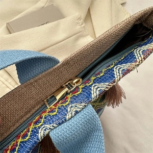 Dettaglio borsa etnica intrecciata con motivi colorati, cerniera dorata e nappine decorative