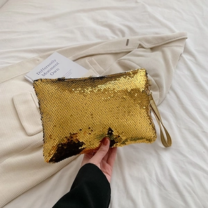 Detail of shimmering gold sequin evening clutch with leather wrist strap on white fabric