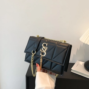 Detail of black quilted shoulder bag featuring gold S-shaped logo and elegant fringe tassel