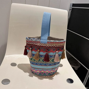 Dettaglio borsa a secchiello intrecciata con motivi geometrici colorati e nappe