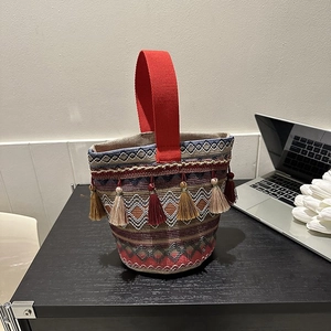 Dettaglio della borsa a secchiello etnica intrecciata con manico rosso e nappe