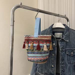 Dettaglio ravvicinato della borsa a secchiello boho tessuta con frange e motivi geometrici