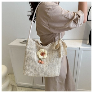 Détail du sac cabas en paille avec fleur en tissu, pompons cerise et nœud en dentelle