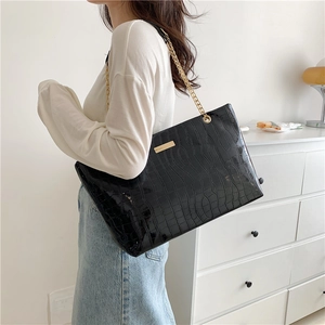 Large black crocodile pattern tote bag with gold chain strap worn by a model