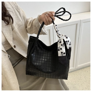 Detail of black houndstooth textured tote bag with woven handle and cherry silk scarf