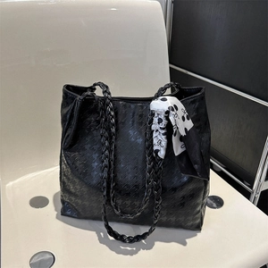 Detail of black tote bag featuring woven leather handles and decorative silk scarf accessory