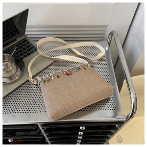 Détail d'un sac bandoulière tissé beige avec pompons en perles colorées et large sangle