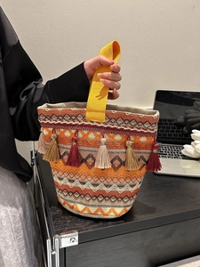 Dettaglio di una borsa a secchiello tessuta boho con nappe colorate e motivi etnici geometrici