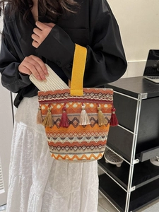 Dettaglio di borsa a secchiello intrecciata arancione con nappe colorate e manico giallo