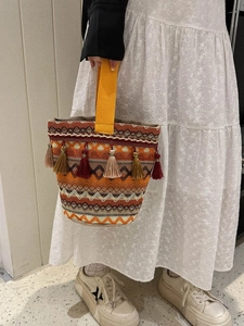 Dettaglio borsa a mano etnica intrecciata con frange colorate e manici giallo zenzero