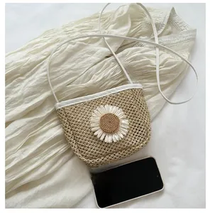 Close-up of beige straw bucket bag featuring a white daisy flower and thin white strap