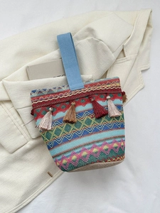 Dettaglio borsa etnica lavorata a maglia con nappe e manico blu appoggiata su libri