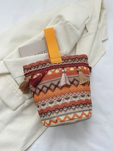 Dettaglio della borsa tessuta bohémien con nappe colorate e ricami su giacca beige