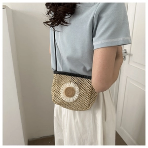 Detail van een beige geweven strooien crossbodytas met een grote witte madeliefjesbloem