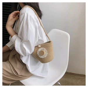 Détail du sac seau en paille tressée avec fleur de marguerite blanche et bouton perle